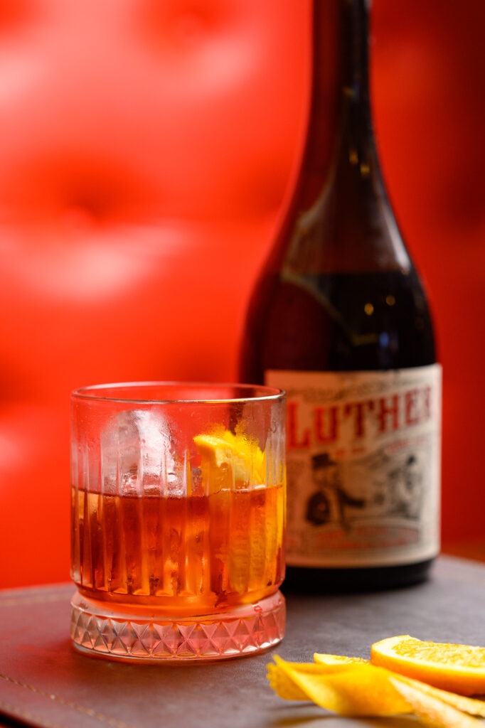 House Negroni over ice with an orange twist, beside a bottle of Luther vermouth